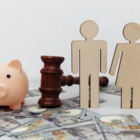 Wooden family figures, gavel and pink piggy bank on dollar banknotes, savings and divorce concept