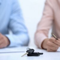 Car keys closeup, couple signing divorce documents about property division Car keys closeup, couple signing divorce documents about property division