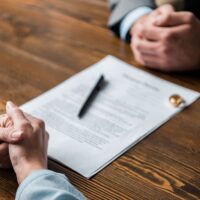 partial view of lawyer and client sitting at table with divorce decree and wedding rings partial view of lawyer and client sitting at table with divorce decree and wedding rings